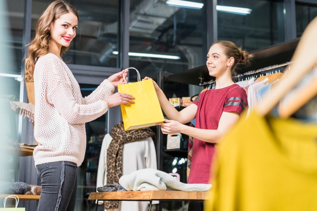 vendedora entregando sacola de compras para cliente